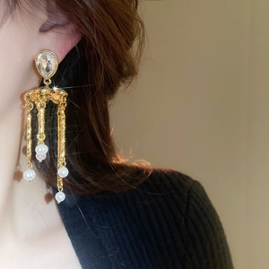 Détail de boucles d'oreilles dorées avec cristal goutte et perles blanches sur un mannequin