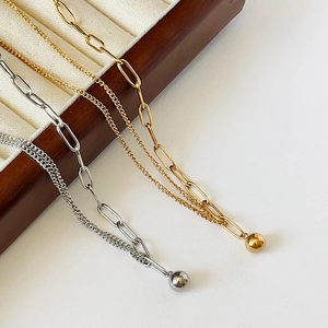 Detail view of asymmetric gold and silver paperclip chain necklace on a wooden jewelry box