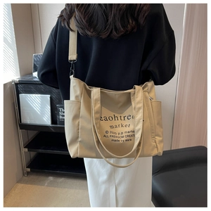 Detail of beige canvas tote bag with black lettering and adjustable shoulder strap