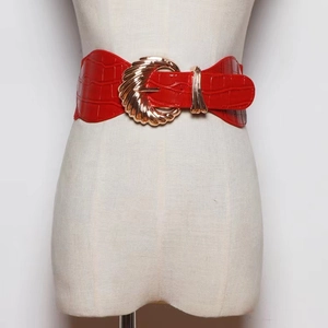 Detail of a wide red crocodile pattern belt with a large golden buckle on a mannequin