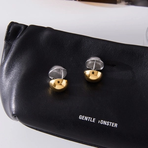 Close-up of two-tone gold and silver hollow sphere stud earrings on black leather texture