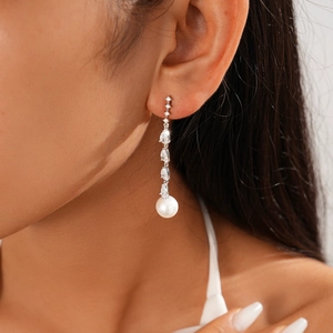 Macro shot of silver drop earrings with zircons and a white round pearl on a model
