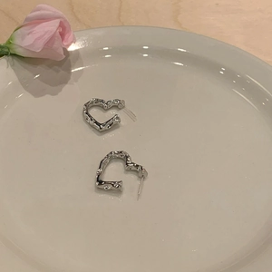 Detail of silver heart hoop earrings with hammered metal texture on ceramic tray