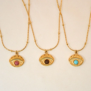 Detailed view of evil eye necklaces in gold with red, brown, and blue stones on fabric