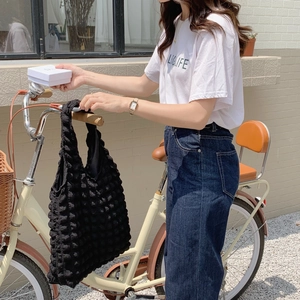 Detail of black popcorn textured tote bag carried by a model on a bicycle