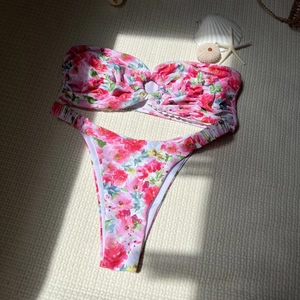 Detailed flat lay of floral bandeau bikini set with starfish and seashell on textured mat