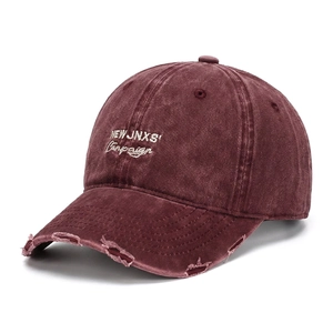 Dettaglio della visiera consumata e del ricamo bianco su un cappellino vintage bordeaux