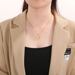 Close-up of a gold-plated necklace featuring a 3D letter H pendant on a model
