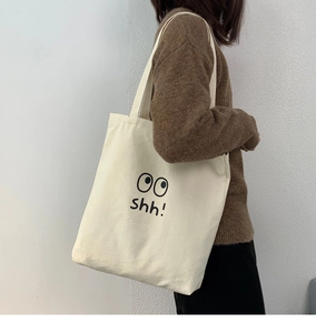 Primer plano de un bolso tote de lona beige con estampado de ojos shh negro