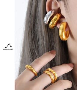 Detail of chunky stainless steel hoop earrings and layered textured gold rings on model