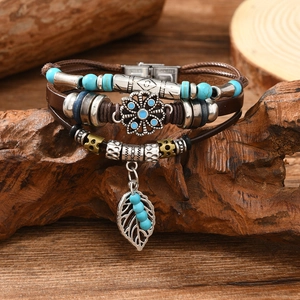 Detail of vintage multilayer leather bracelet with leaf pendant and turquoise beads on wood