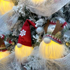 Close-up of glowing Christmas gnomes with warm LED lights and knitted hats on a tree