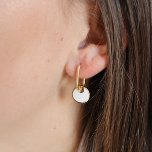 Detail of gold circular hook earring with white shell disc pendant on model's ear