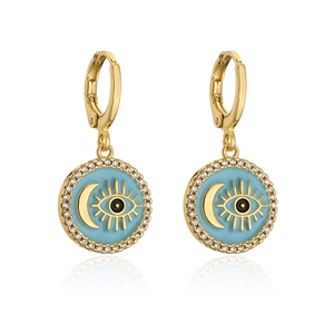 Macro shot of gold-plated geometric earrings featuring blue enamel eye and crescent moon motifs