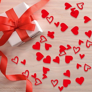 Red heart confetti and a white gift box with a red ribbon on a light wooden background