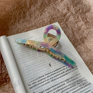 Macro detail of large acetate claw clip with colorful resin and gold metal teeth on a book