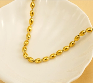 Macro view of gold-tone oval bead necklace displayed on a white shell ceramic plate
