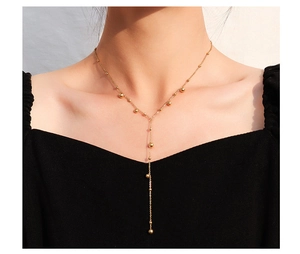 Detailed view of a gold-toned Y-shaped tassel necklace with small beads worn on a black top