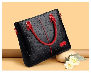 Detail of black embossed leather tote with red handles and textured pattern finish