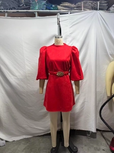Détail d'une robe rouge en suédine avec manches bouffantes et ceinture fleur dorée