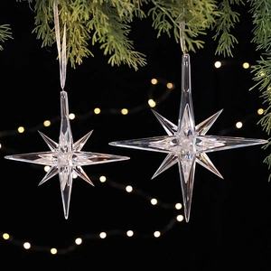 Clear acrylic star ornaments hanging on Christmas tree branches with warm festive lighting