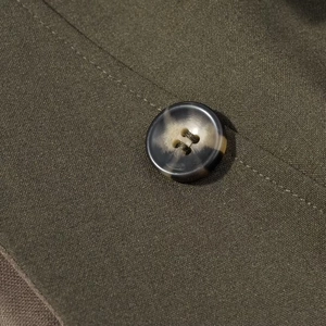 Macro shot of olive green woven fabric with a tortoiseshell pattern four-hole button detail