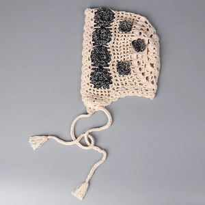 Detail of crochet baby hat with black flower patterns and long braided tassels