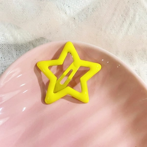 Detail of a bright yellow star-shaped metal hair clip on a pink textured plate