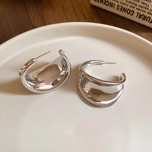 Close-up of silver C-shaped liquid metal earrings on a minimalist ceramic plate