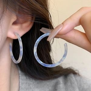 Macro shot of large blue and white marble-patterned C-shape hoop earrings worn by a model
