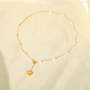 Minimalist pearl necklace with heart pendant and gold beads on satin background
