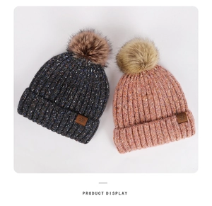 Detailed close-up of knit hats with fuzzy pom-poms and snowflake leather patches