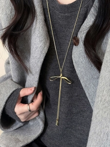 Close-up of a golden bow pendant necklace with elegant dangling tassels on a gray coat