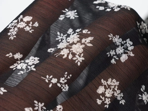 Detailopname van zwarte mesh-stof met delicate witte bloemenprint en textuur