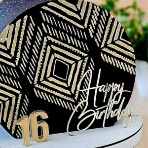 Macro shot of gold acrylic 16th Happy Birthday cake toppers with black and gold patterns