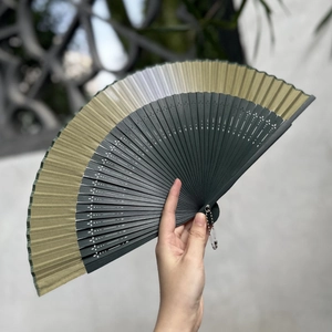Chinese style dark green and gold folding fan with decorative bamboo ribs and pendant