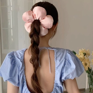 Rear view of a large pink fabric flower scrunchie on a model's braided ponytail