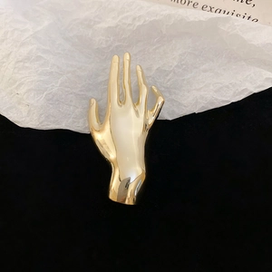 Polished gold hand-shaped brooch displayed on a high-contrast black and white backdrop