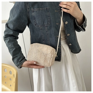 Detail of beige straw woven crossbody bag with long strap shown on model's shoulder