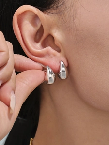 Close-up of silver hollow teardrop earrings with high-polish mirror finish on earlobe