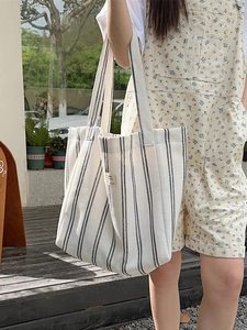 Large canvas tote bag with navy blue vertical stripes shown in an outdoor lifestyle setting