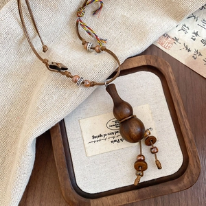 Detailed view of handcrafted ethnic wooden gourd pendant on a brown braided necklace