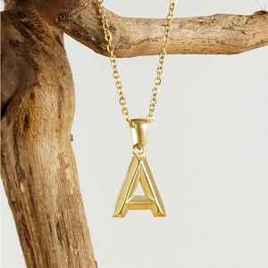 Detailed view of golden 18K letter A pendant necklace on a natural wooden branch