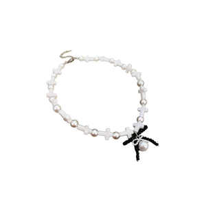 Cross pearl necklace with black ribbon bow pendant and crystal accents on white background