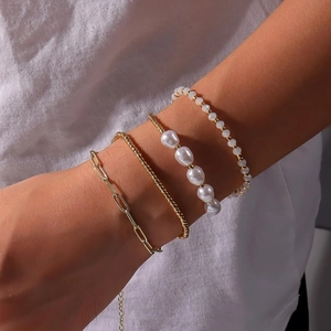 Détail de bracelets superposés avec chaîne trombone dorée et perles blanches pour femme
