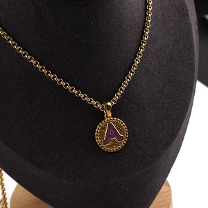 Detailed view of a gold chain necklace with a purple letter A pendant on a black bust