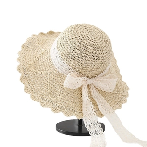 Women's beige straw sun hat featuring elegant white lace bow and wavy brim design