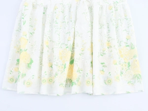 Detailed close-up of white floral dress hem with yellow embroidery and pleated texture