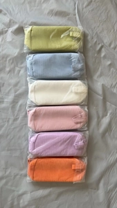 Vertical row of six corduroy makeup bags in pastel colors with individual clear packaging