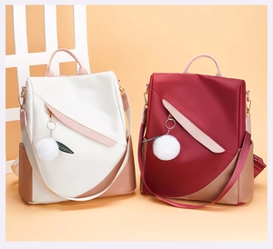 Detail of cream and burgundy backpacks with fluffy pompom and leaf charms on the zippers